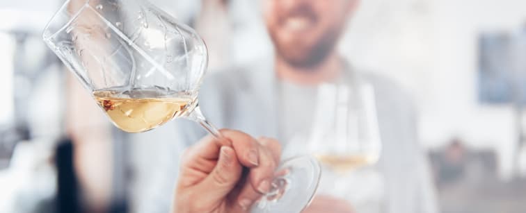 Närbild av ett vinglas fyllt med vitt vin, med en suddig bakgrund i mjuka, varma toner.