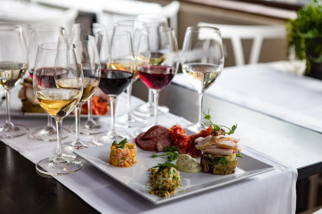 Flera glas med vitt, rött och rosévin uppställda bakom tallrikar med små aptitretare och charkuterier, redo för vinprovning med tilltugg.