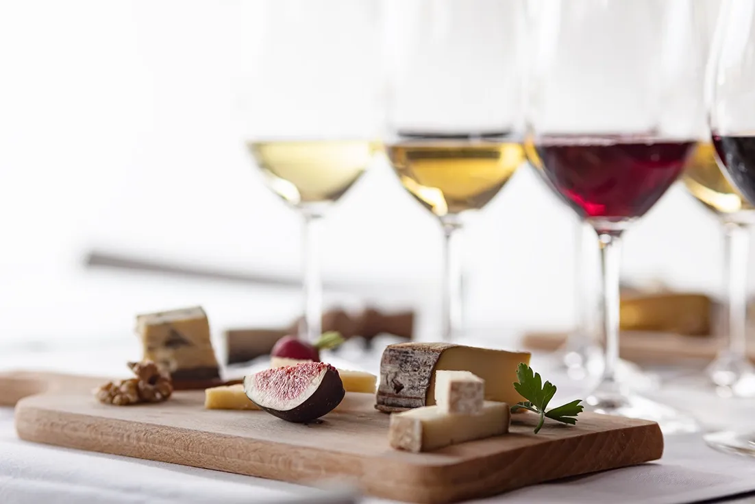 Ostbricka med olika sorters ost, fikon och nötter, uppställd framför glas med vitt och rött vin, redo för vin- och ostprovning.
